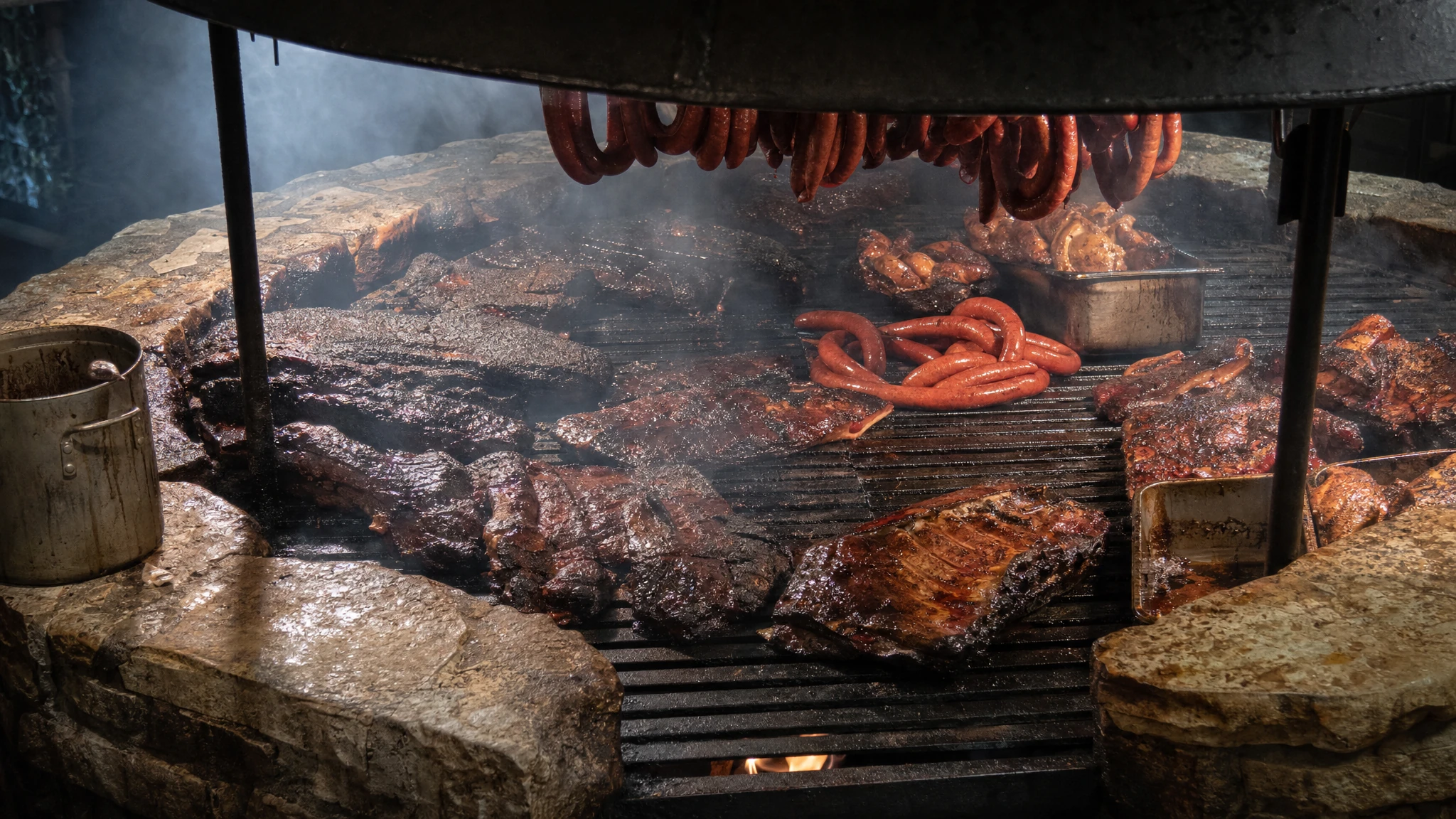 Brisket and sausages cooking over the Salt Lick Driftwood barbecue pit