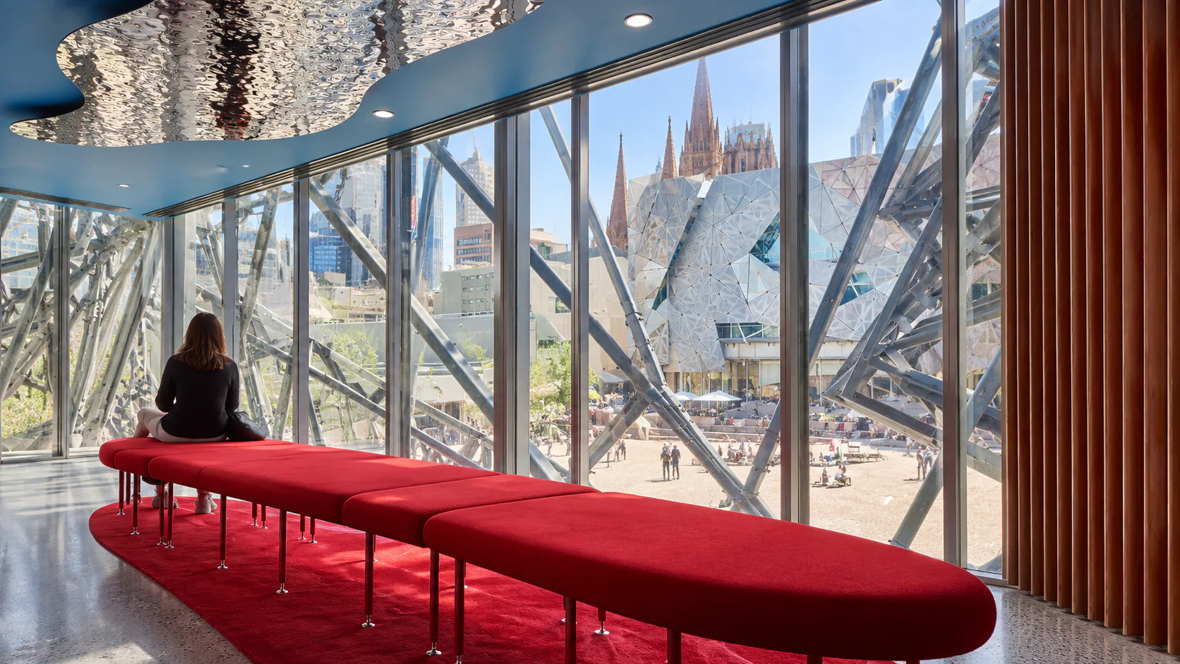 Red window-side seating overlooking Federation Square inside Koorie Heritage Trust