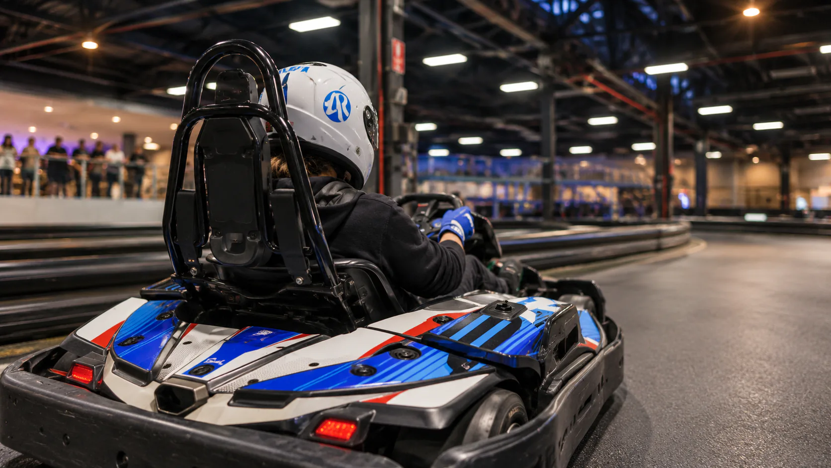 A driver in a blue, white and red kart at Auscarts Racing's indoor track.