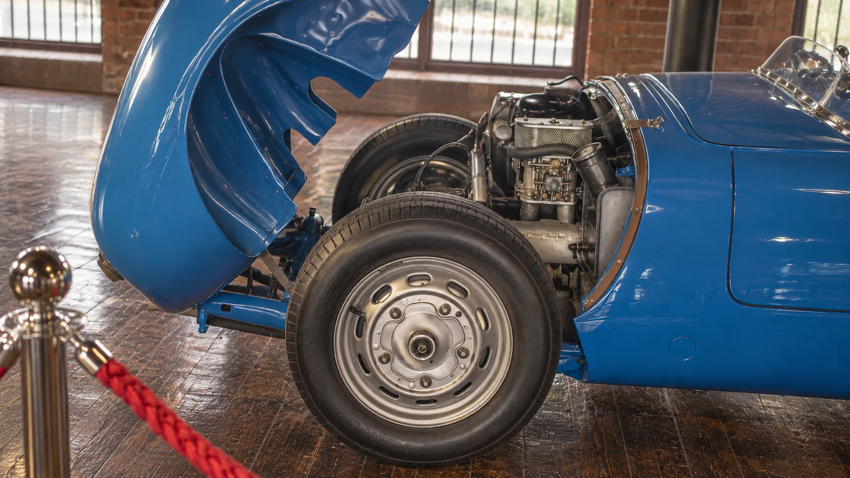 The raised bonnet, exposed engine and front wheel of a blue classic roadster in the Fox Collection.