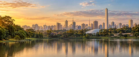 Destination artwork of São Paulo: São Paulo skyline beyond Ibirapuera Park lake, lush green parkland in foreground, modern Brazilian urban towers and warm early evening light.