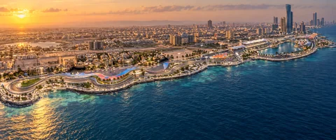Destination artwork of Jeddah: Jeddah Corniche circuit alongside the turquoise Red Sea, sinuous coastal racetrack and waterfront, warm golden hour light.