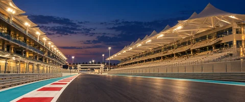 Destination artwork of Abu Dhabi: Yas Marina Circuit at blue hour, illuminated pit straight with white canopy grandstands and turquoise trackside accents.