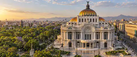 Destination artwork of Mexico City: Mexico City's Palacio de Bellas Artes beside the green Alameda Central park, its warm orange and gold dome and elegant white marble facade in clear late afternoon light.
