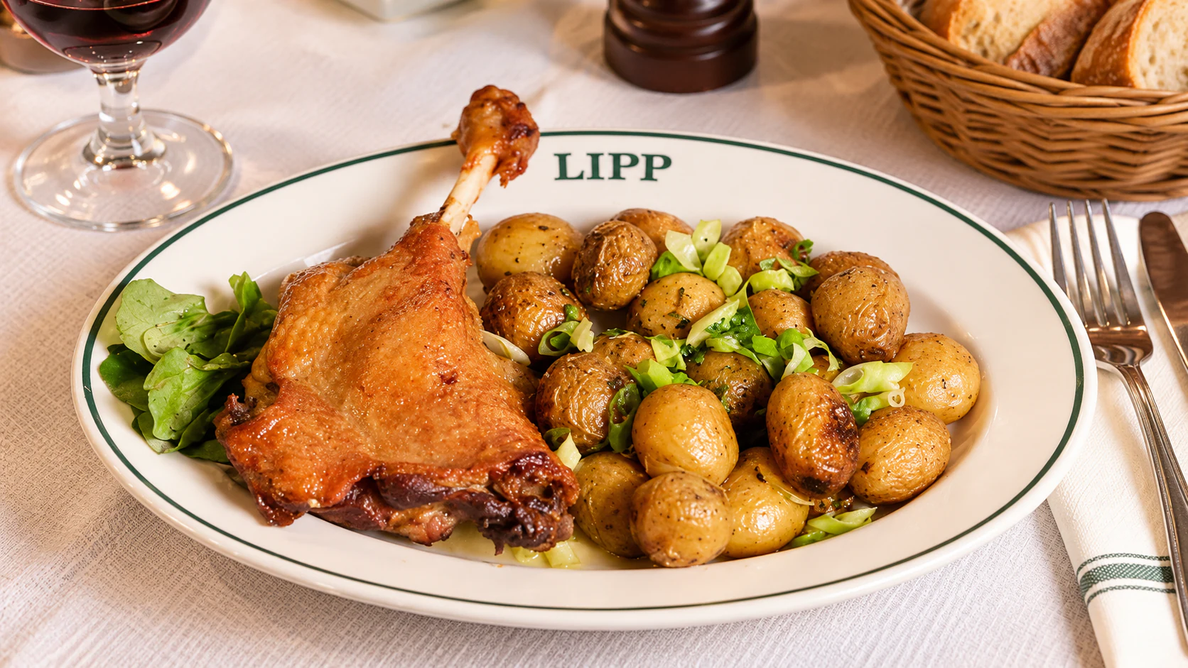 Confit duck leg with browned potatoes and green leaves, served on a Lipp oval plate.
