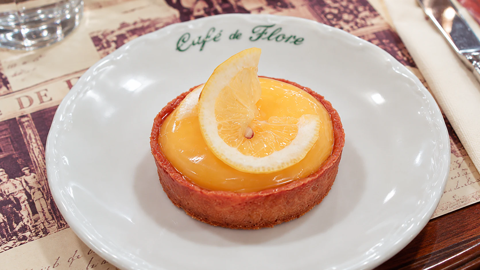 Lemon tart with a smooth yellow filling and a thin lemon slice on top, served at Café de Flore.