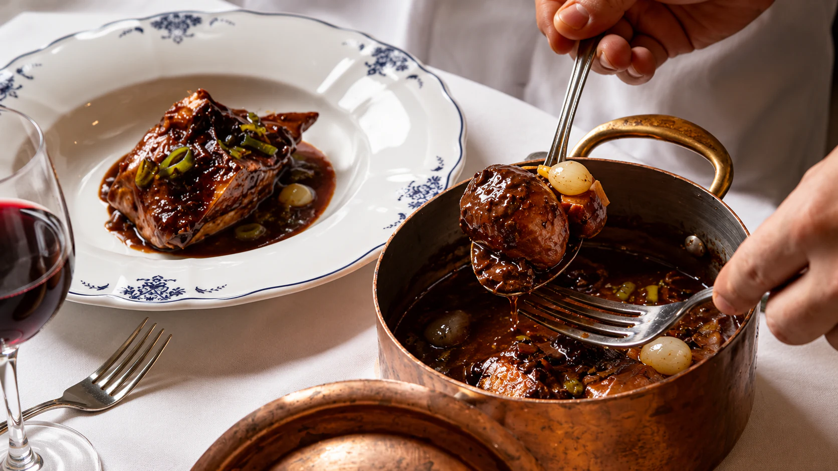 Coq au vin “Ivre de Juliénas”, with dark wine sauce served from a copper casserole.