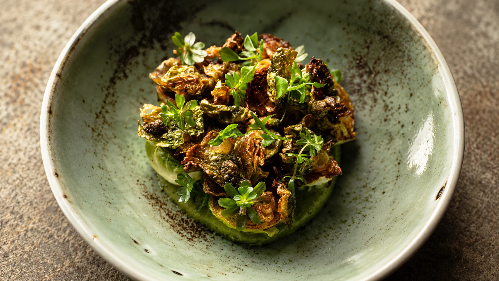Roasted Brussels sprouts and fresh herbs on a green ceramic plate at David Toutain