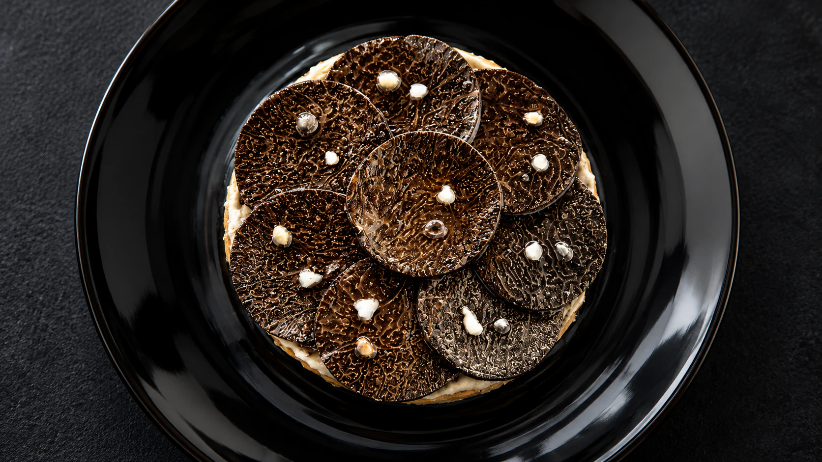 Overlapping black-truffle slices on a dark plate at Le Jules Verne