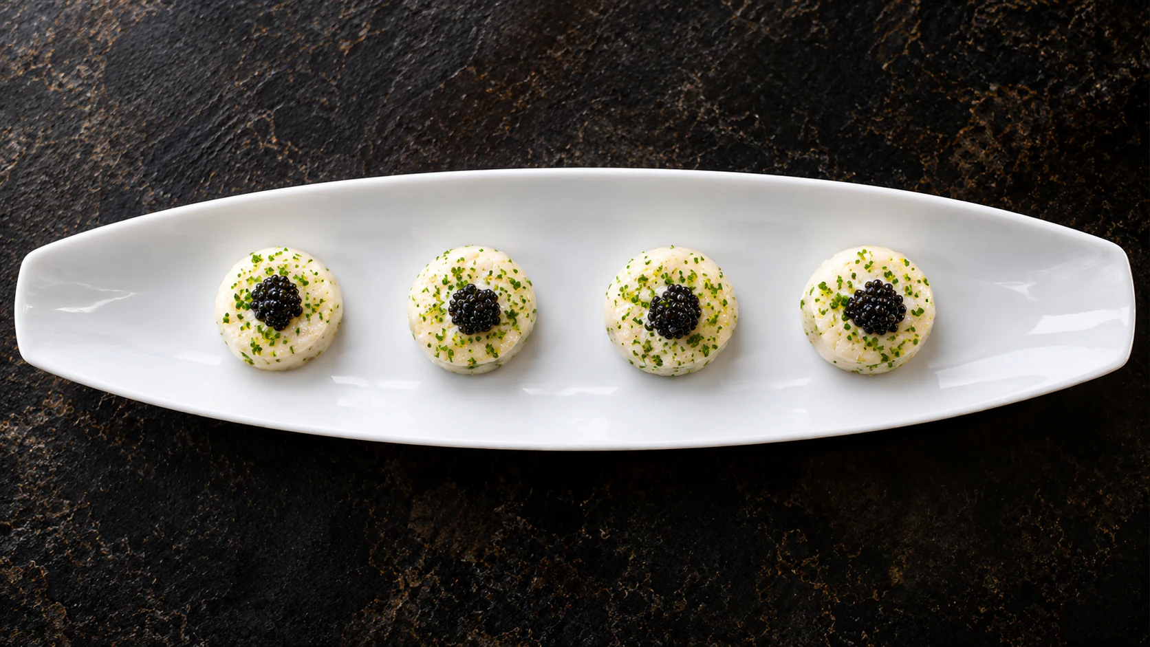 Four caviar-topped small bites on a long porcelain platter at Le Jules Verne